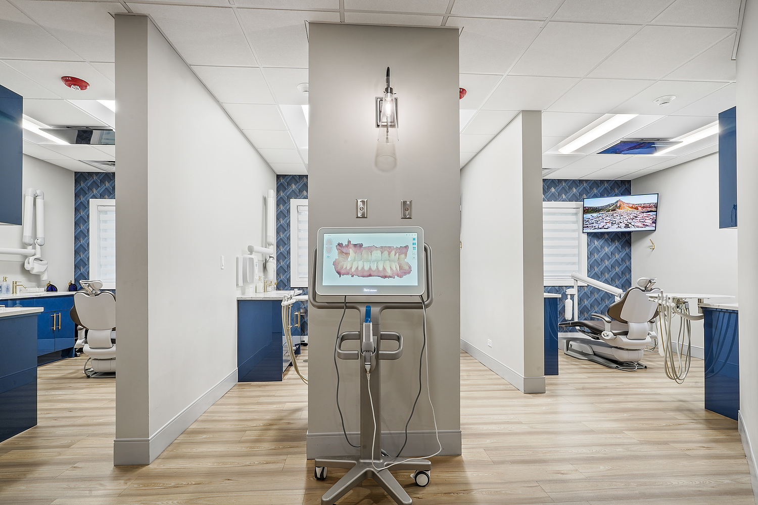 An interior view of a modern dental office with a blue and white color scheme, featuring dental chairs, equipment, and a waiting area.