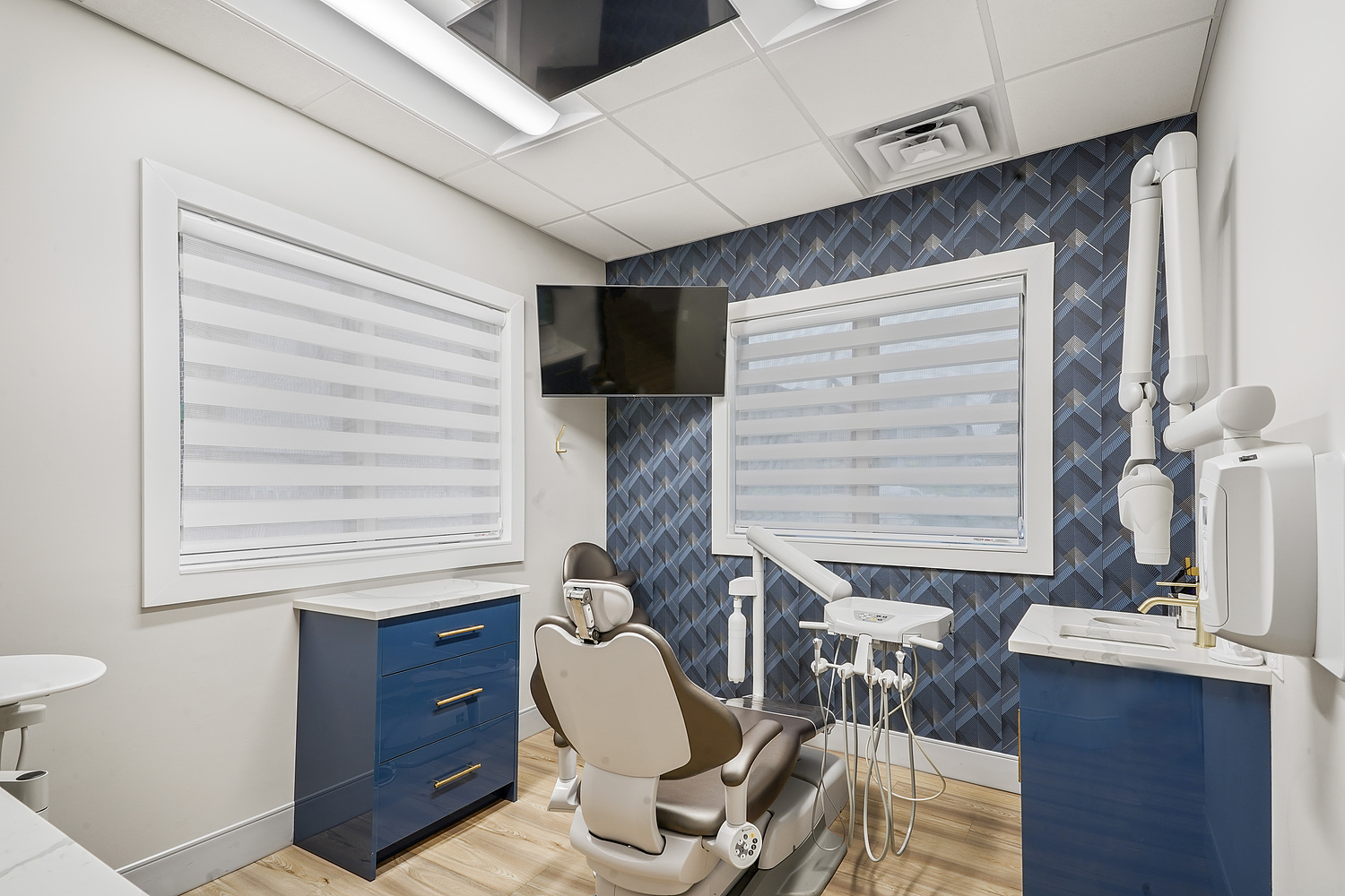 The image shows an interior view of a dental office with modern furnishings, equipment, and decor.