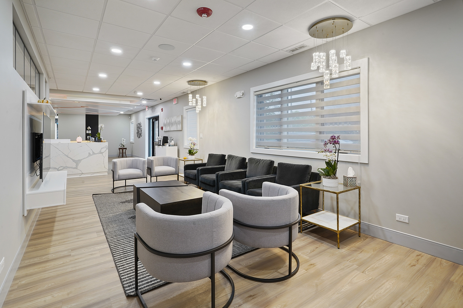 The image shows a modern, well-lit interior space with a contemporary design, featuring a reception area with seating, a coffee table, and a waiting area.