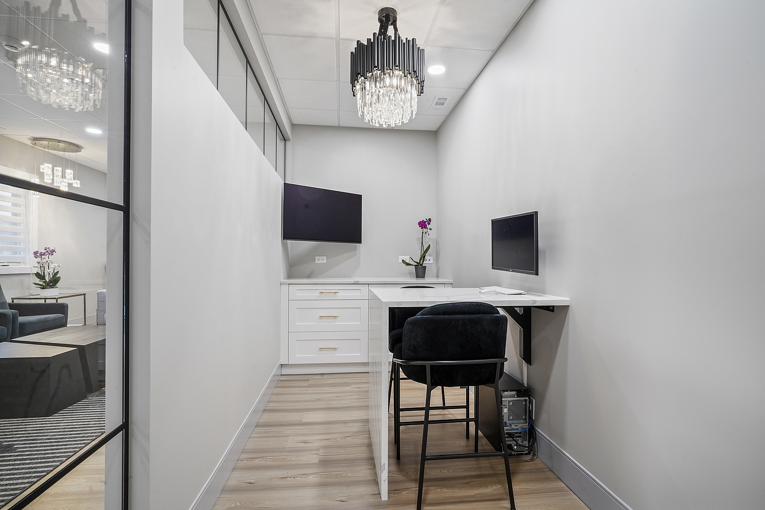 The image shows a modern office interior with a desk, chair, and television monitor against a white wall.