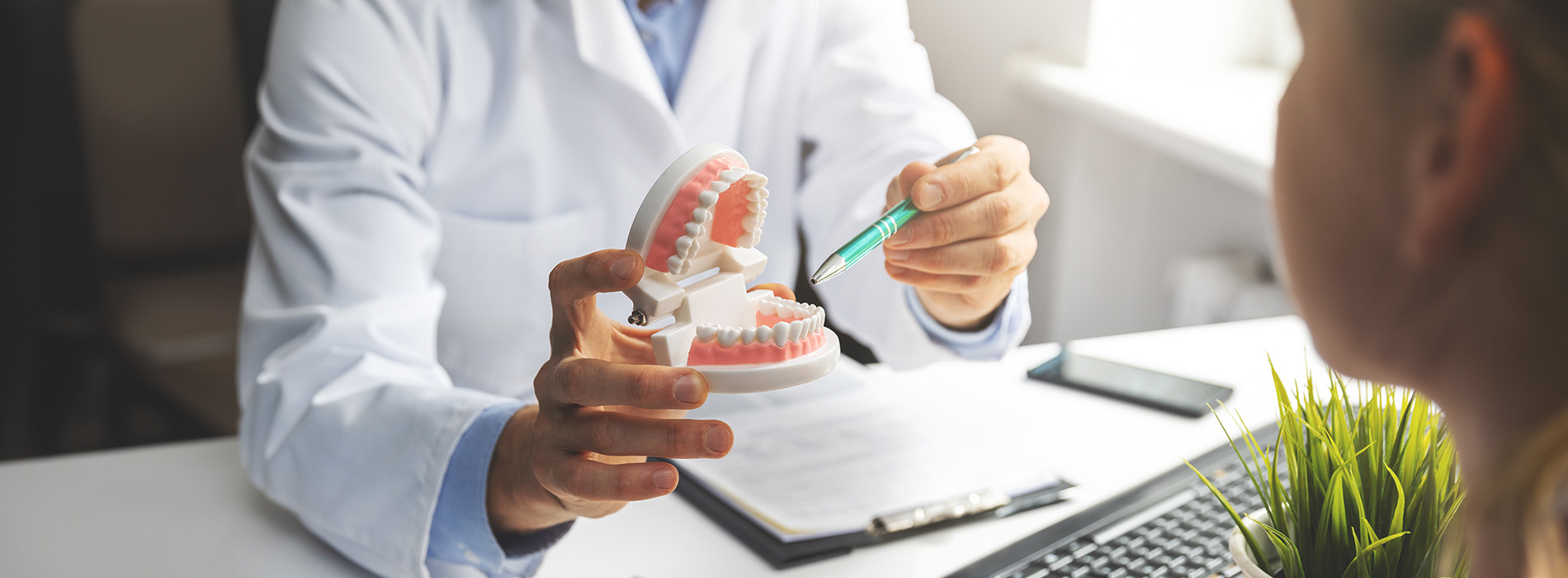 The image shows a professional setting with a dentist examining a patient s mouth, using a dental mirror to inspect the teeth.