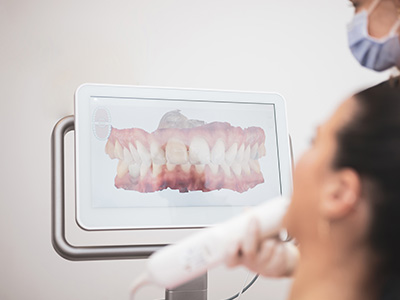 The image shows a person using a digital dental scanner, with a 3D model of a tooth displayed on the screen.