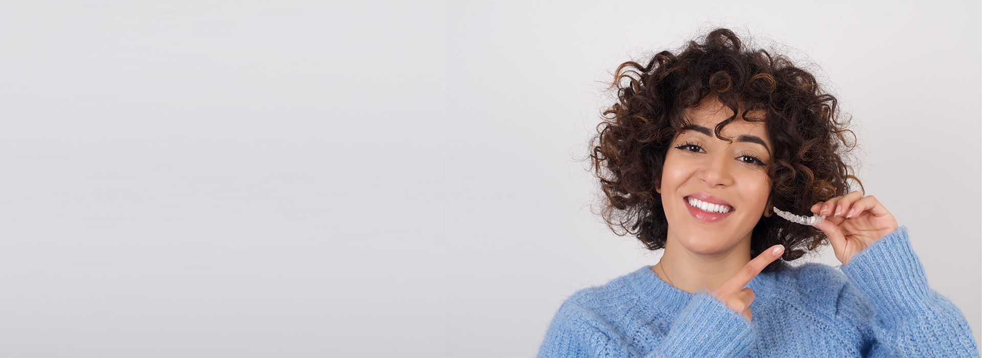 The image shows a woman with curly hair smiling at the camera, wearing a blue top and holding a phone to her ear.