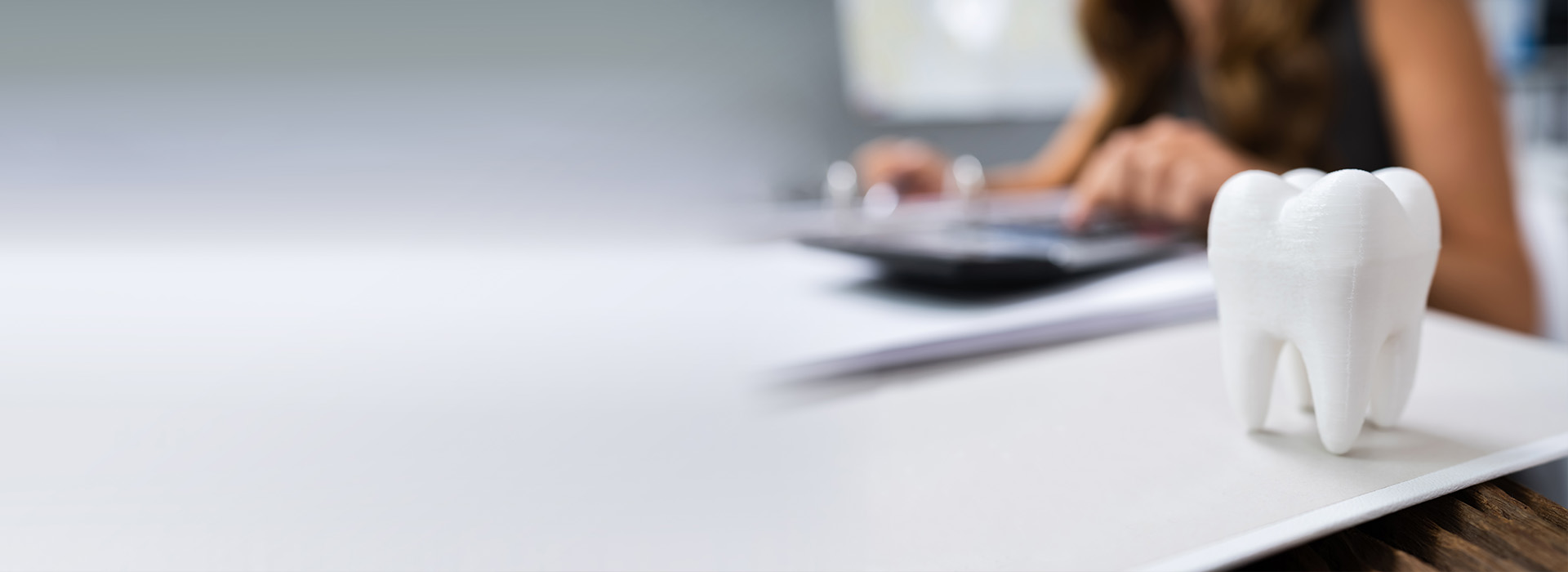 The image shows a person working at a desk with a computer, papers, and a toothbrush-shaped object in the foreground.