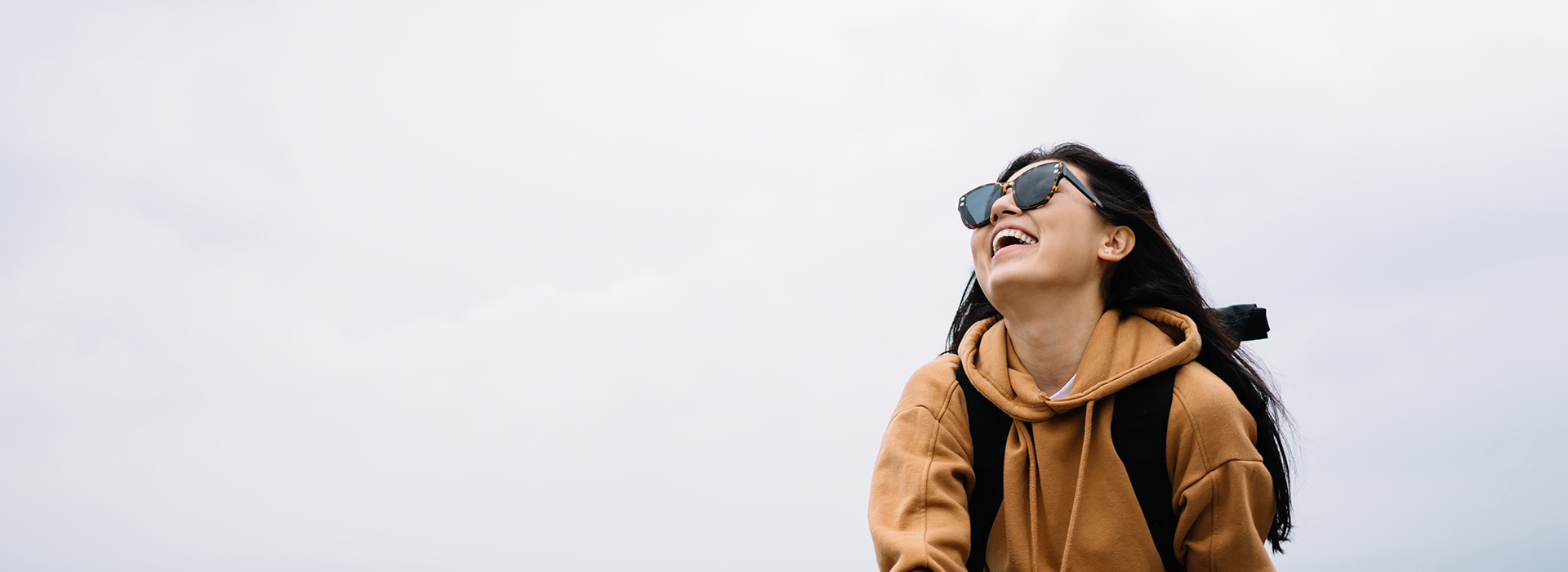 A person stands outdoors, smiling at the camera, with a backpack and sunglasses.