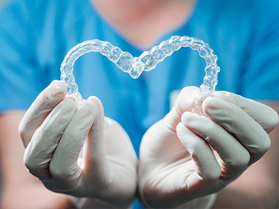 The image shows a person s hands holding a transparent, heart-shaped object that resembles a dental appliance or mouthguard.