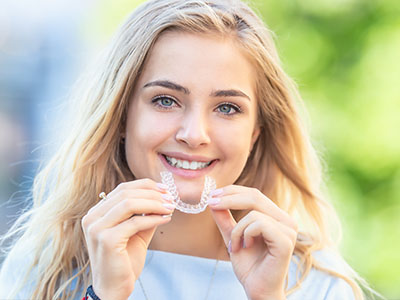 A smiling woman holding a clear dental retainer, showcasing a toothy grin.