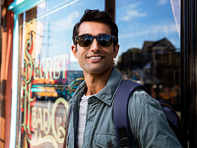 A man with sunglasses, holding a backpack, stands in front of a store window.