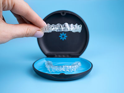 The image shows a person s hand holding an open case containing clear aligners, which are used for orthodontic treatment.