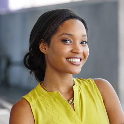 A smiling woman with a yellow top, posing against a backdrop of a building.