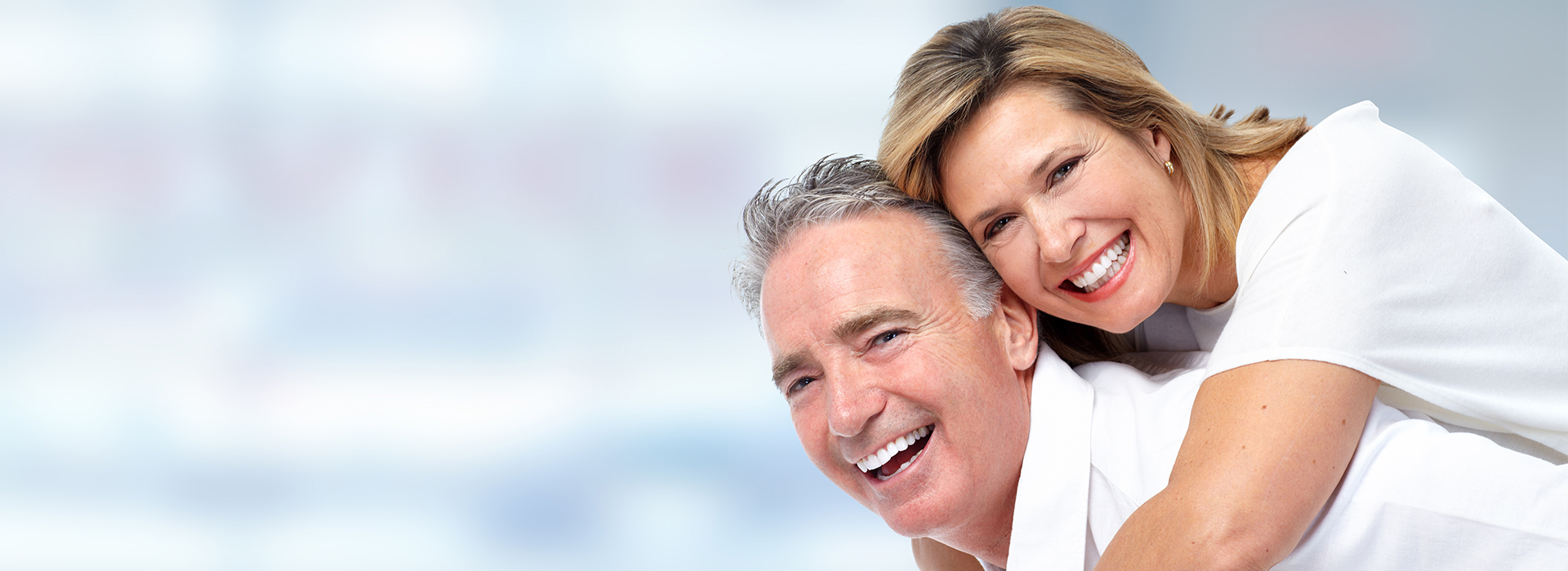 The image features a man and woman, both smiling, embracing each other from behind. They are looking out towards something beyond the frame of the photo.