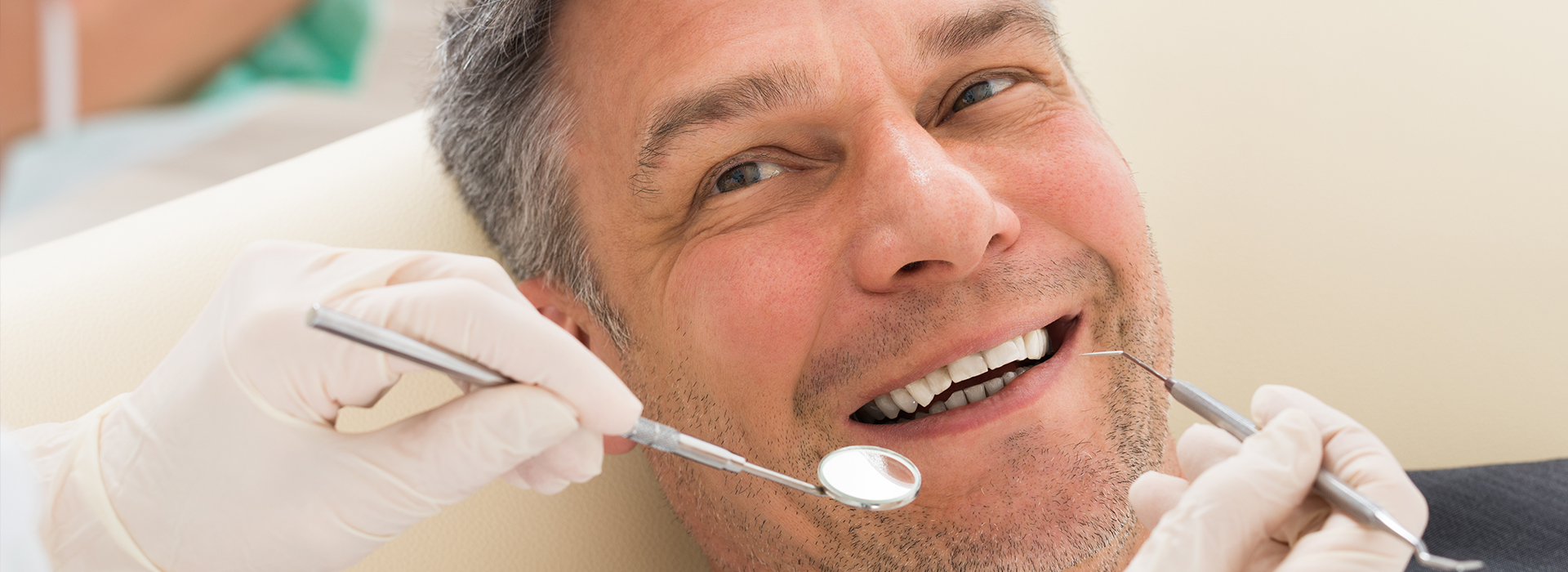 A man in a dental chair receiving dental treatment, with a smiling expression and a dental hygienist working on his teeth.