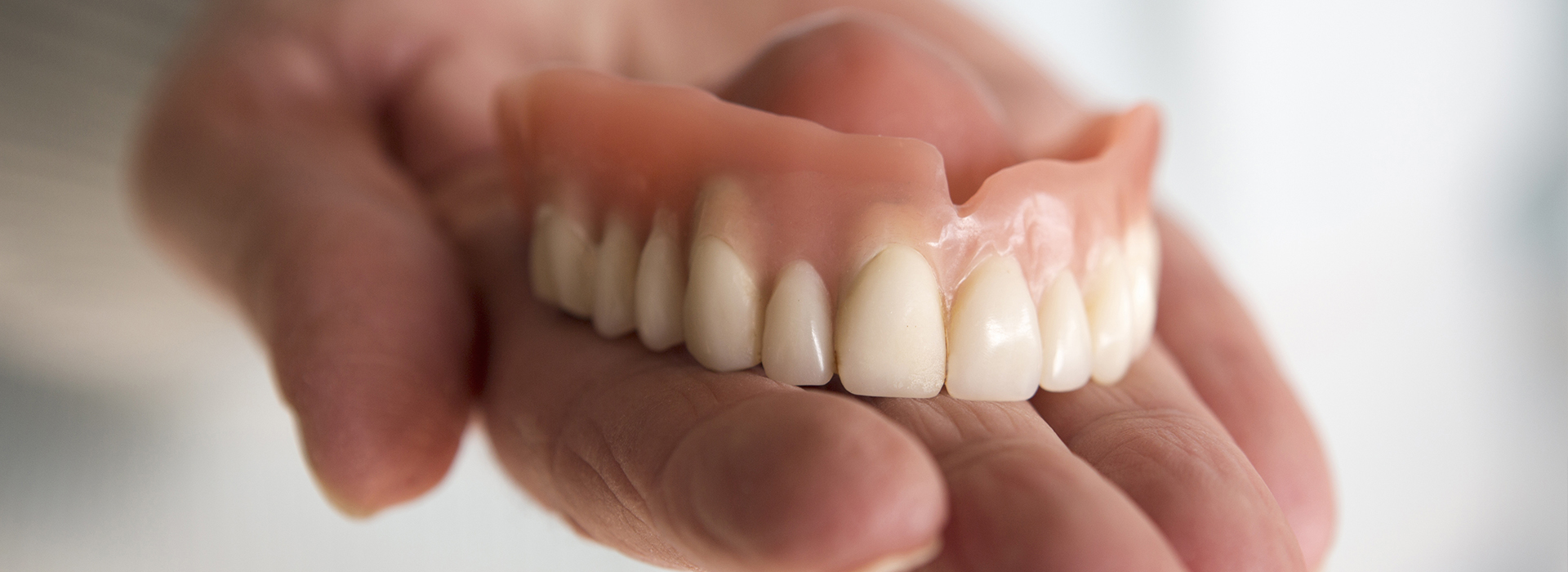 Person holding a set of dentures with visible teeth and gums.