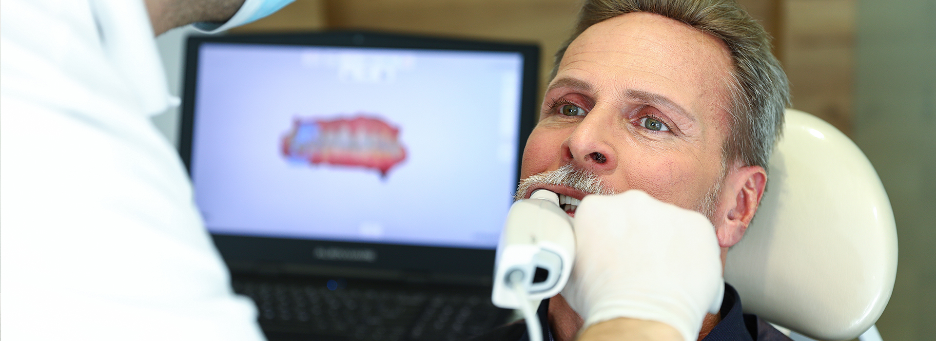 A man is receiving dental treatment in a professional setting, with a dentist using a computer screen to guide the procedure.