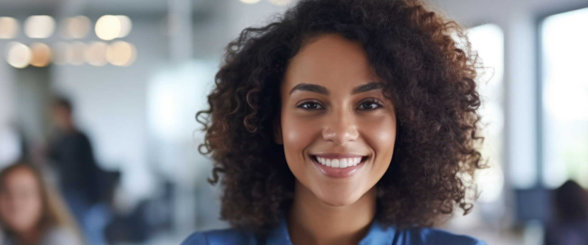 A person with a warm smile, standing in an office environment.