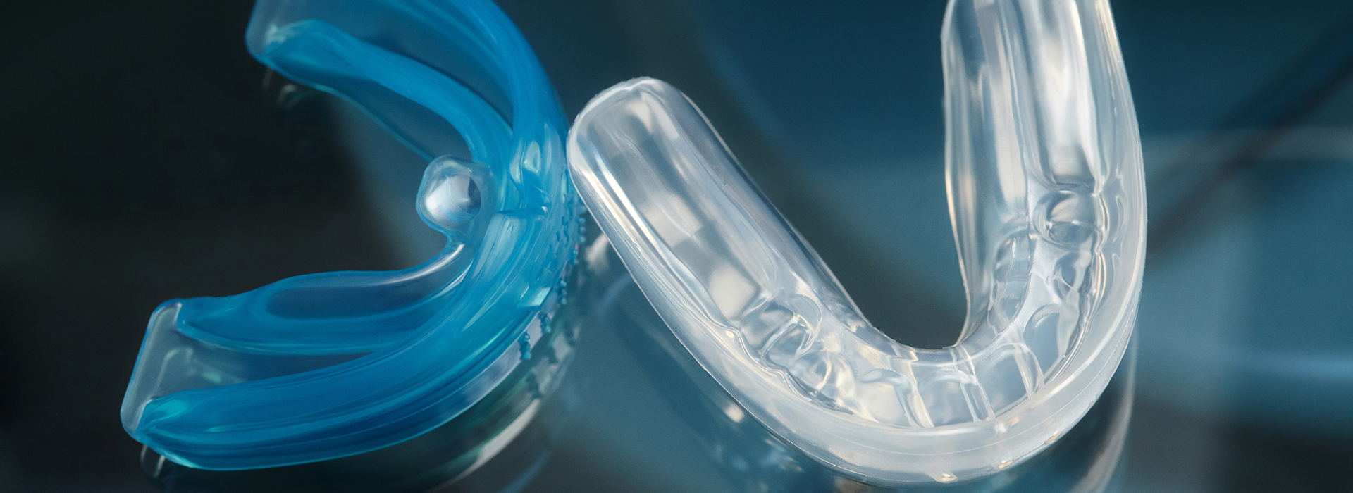 The image displays a close-up of two clear, plastic braces with a blue elastic band, set against a blurred background.