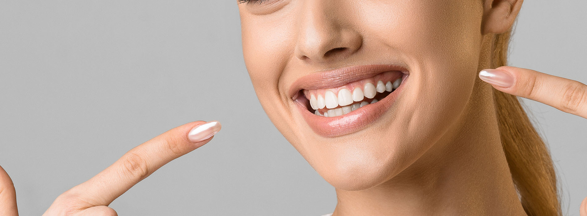 A smiling woman with a manicure gesturing towards her nails with both hands.