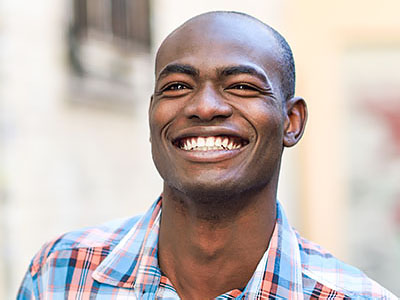 The image shows a smiling man with short hair, wearing a plaid shirt.