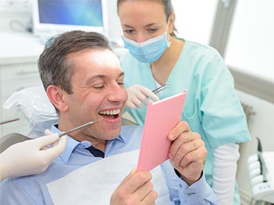 Man in a dental chair, holding up a pink card with a smile, surrounded by dental equipment and professionals.