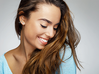 The image features a young woman with long hair, smiling at the camera. She has fair skin and is wearing a light blue top.