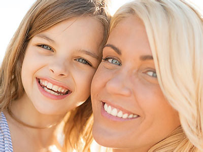 A smiling woman and young girl, both with light hair, sharing a joyful moment together.