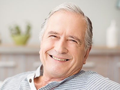 The image shows an elderly man with a smile, wearing glasses and sitting in a relaxed pose.