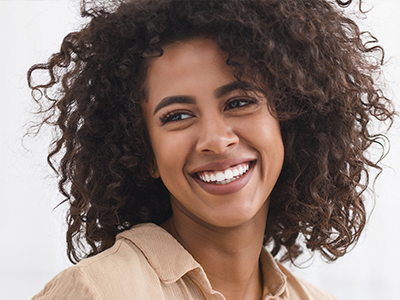 A woman with curly hair and a radiant smile, wearing a white top and beige pants.