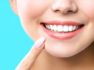 A close-up of a smiling woman with fair skin, showcasing her teeth and applying lipstick.